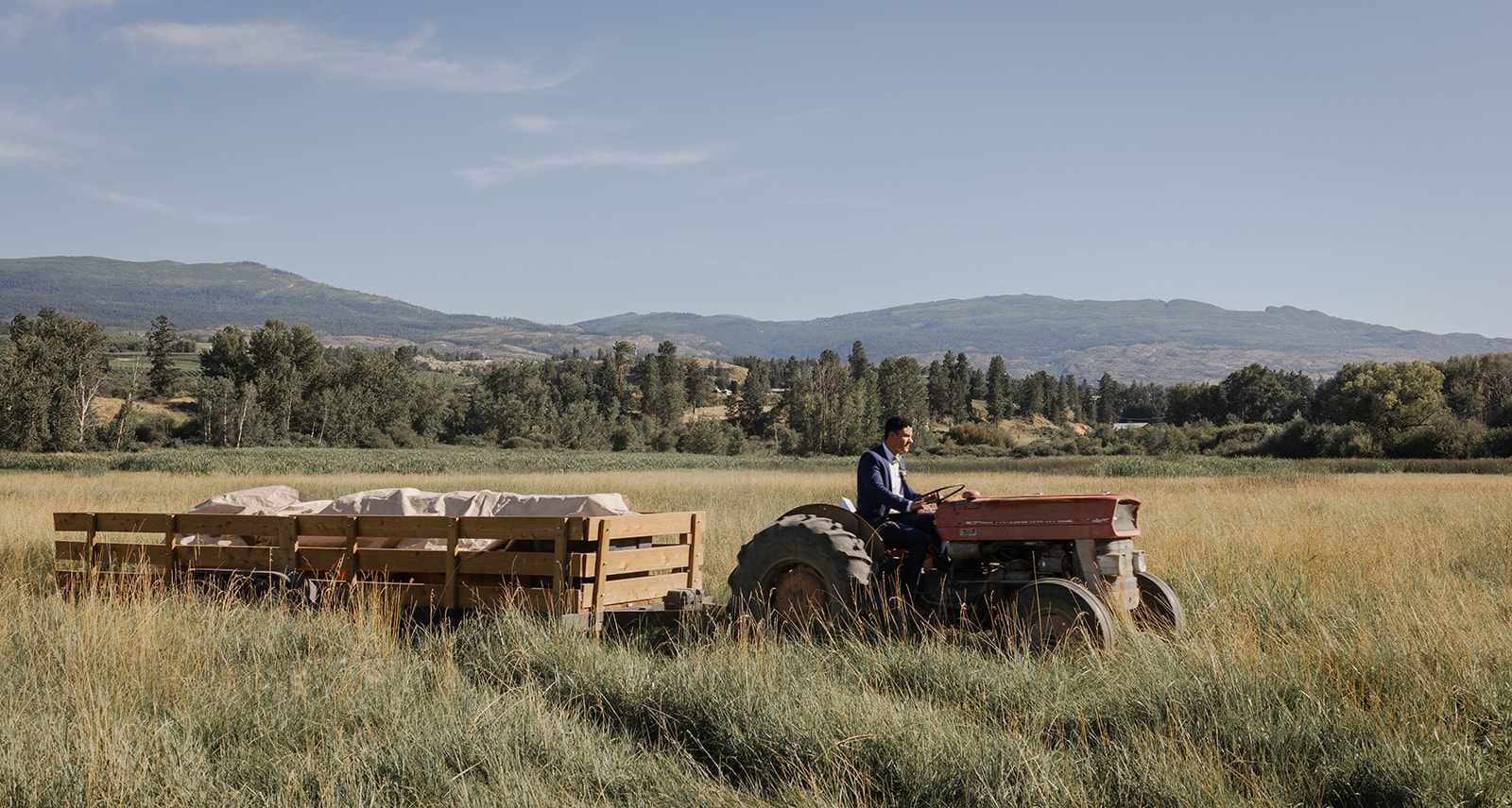 farmer riding a tractor in a field pulling a trailer