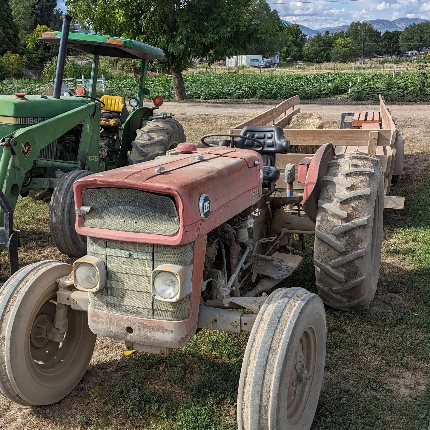 a red tractor next to a green tractor, both with trailers